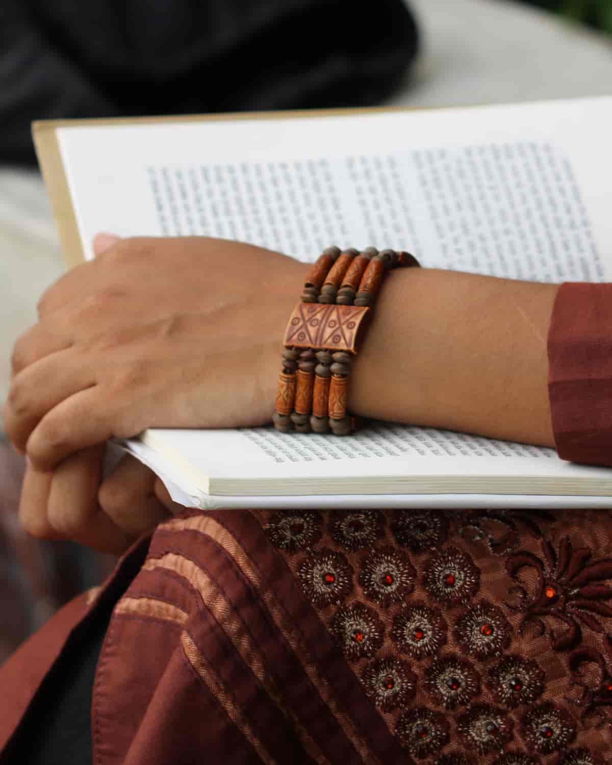 Dr K. Anitha’s hands resting on an open book, a wooden bangle at the wrist, an embroidered kurta sleeve.