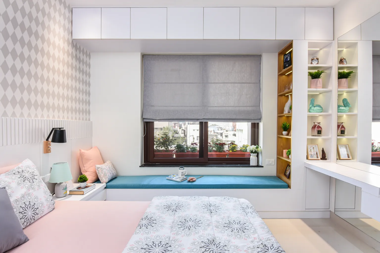 A bedroom wall built as white wardrobes and open teak shelves around a window, a seat under the window.