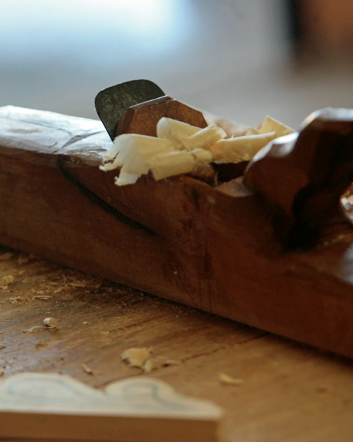 An old wooden plane resting in fresh shavings on the bench.