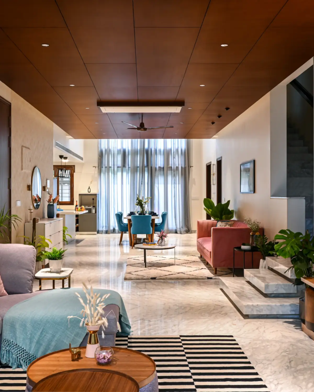 The ground floor, a long marble hall under a teak ceiling: sofas and a round table in front, a dining set beyond.