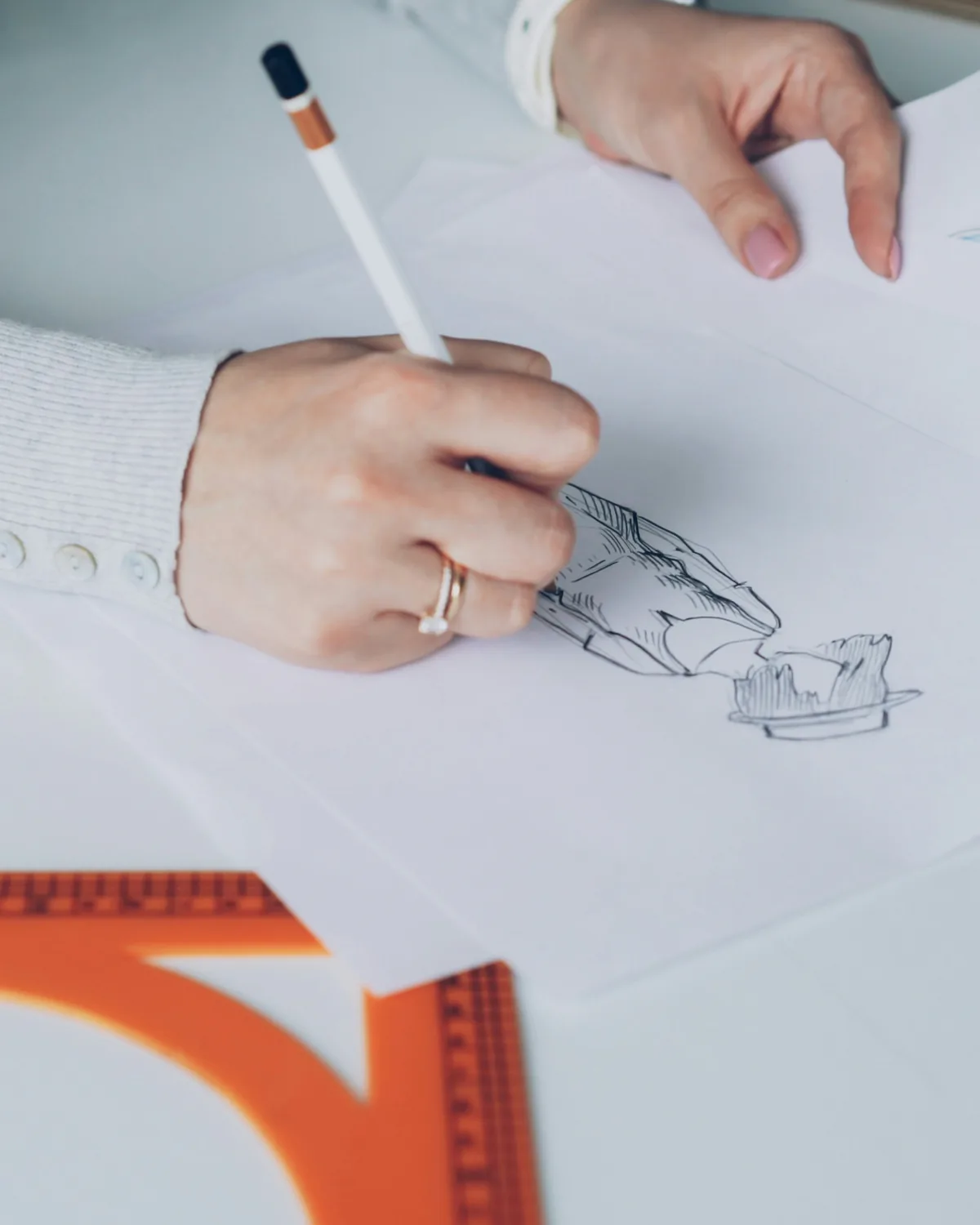 A woman's hands at a drawing, a pencil and a set square beside them.