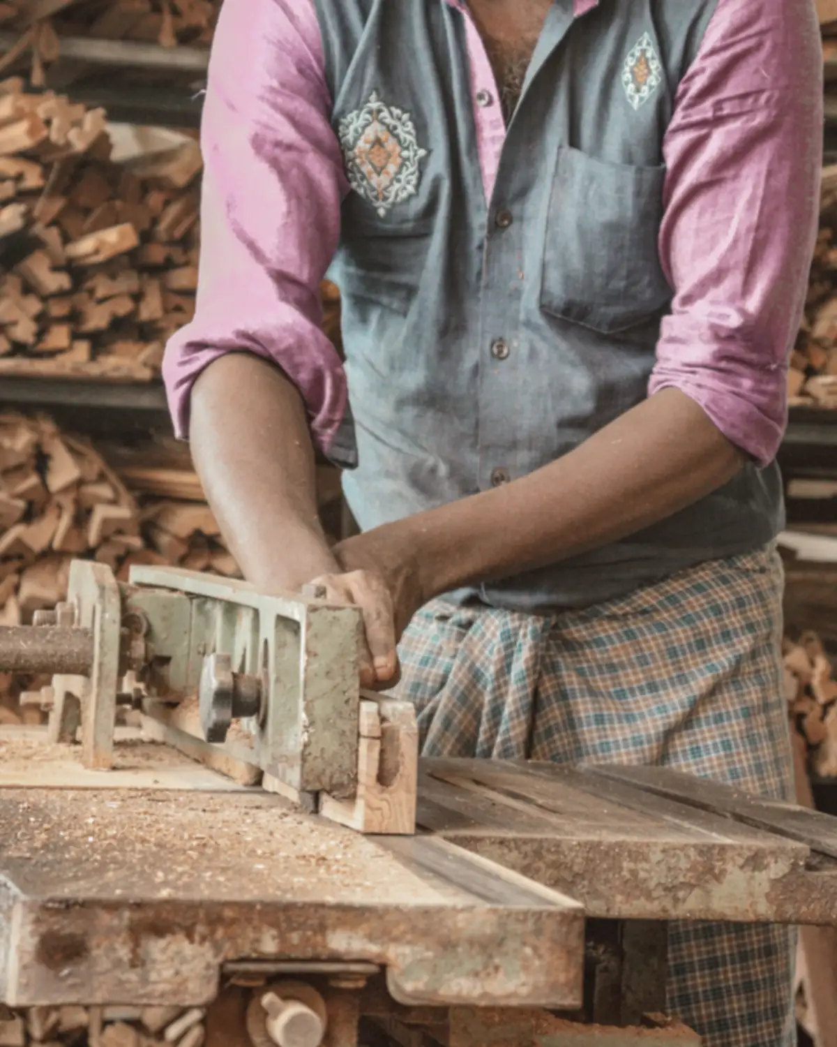 A man at the bench planing a plank, seen from the chest down.