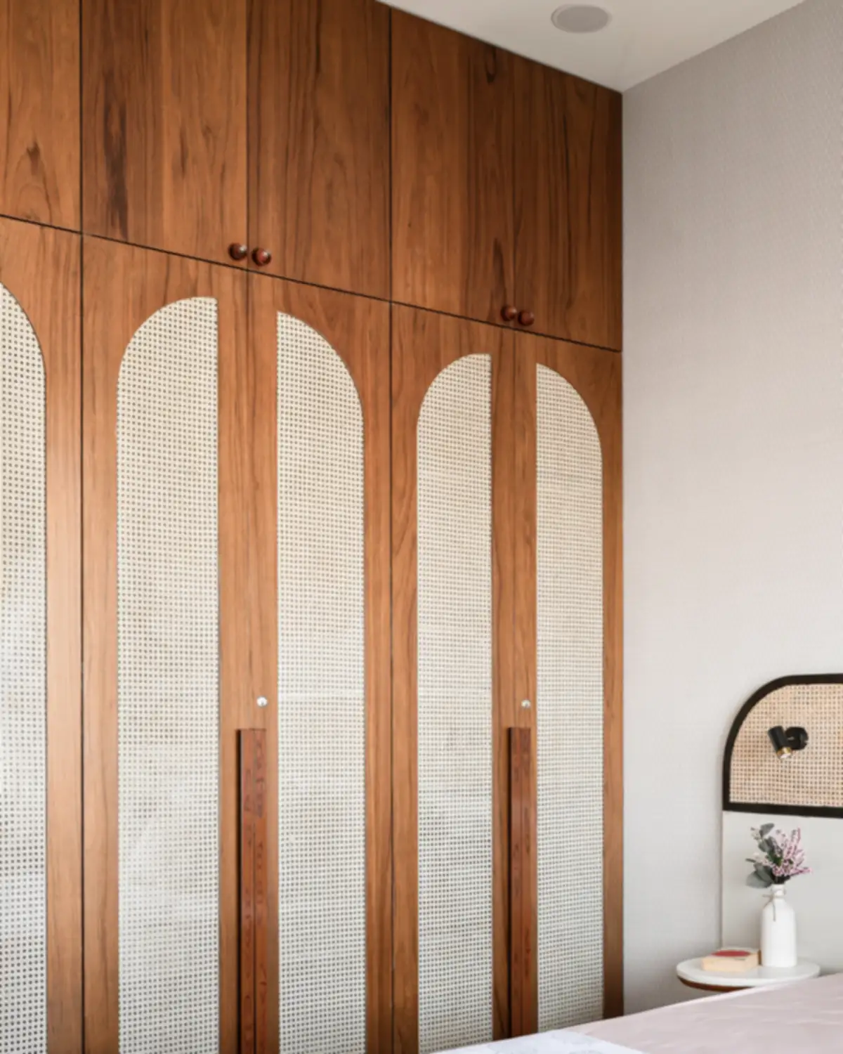 A floor-to-ceiling teak wardrobe, cane panels set into four arched doors.