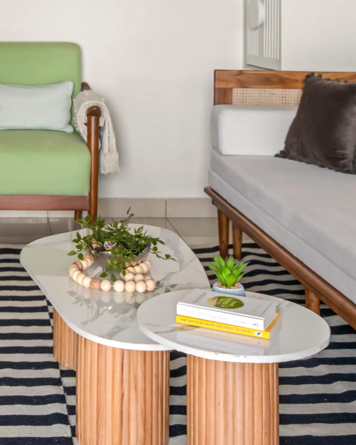 Two oval coffee tables, white marble tops on fluted teak drums, on a striped rug.