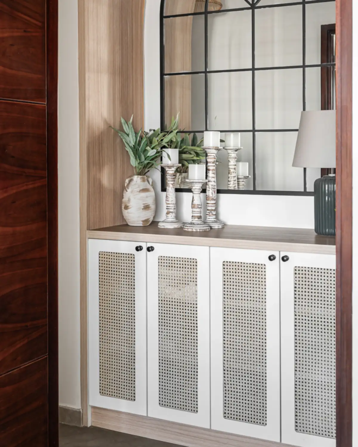 A white console with four cane doors under an arched window mirror, vases on top.