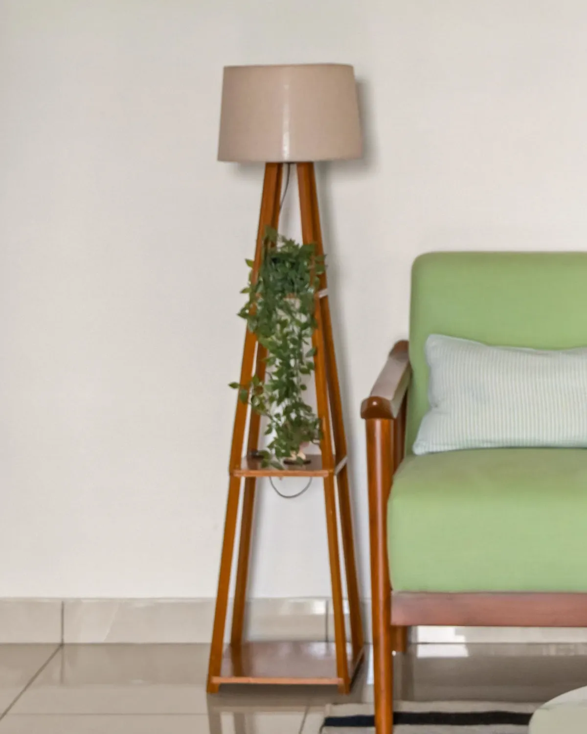 A teak tripod floor lamp with a linen shade, a trailing plant on its shelf.