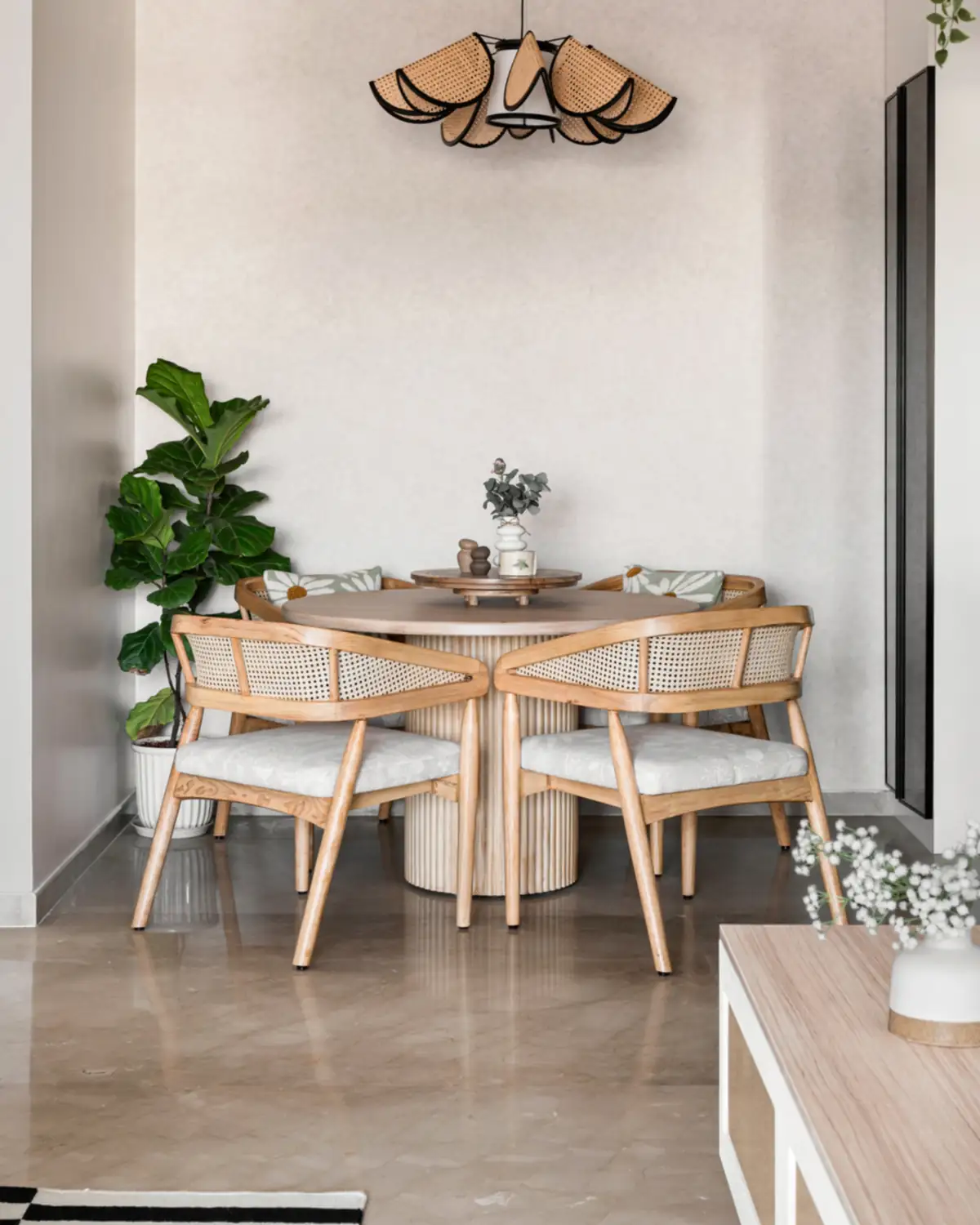 A round four-seater dining table on a fluted pedestal, cane-backed chairs around it, a wooden pendant above.
