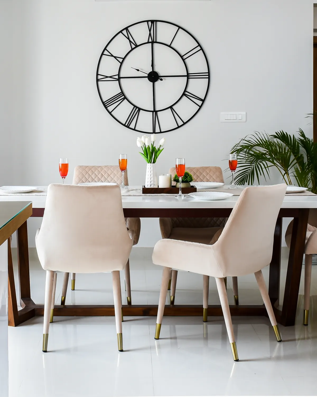 A six-seater dining table, a white marble top on a sheesham trestle base, cream velvet chairs around it.