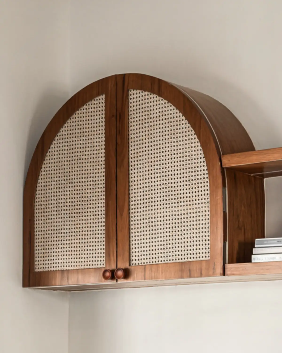 A wall-hung teak cabinet, two cane doors under an arch, a shelf beside it.