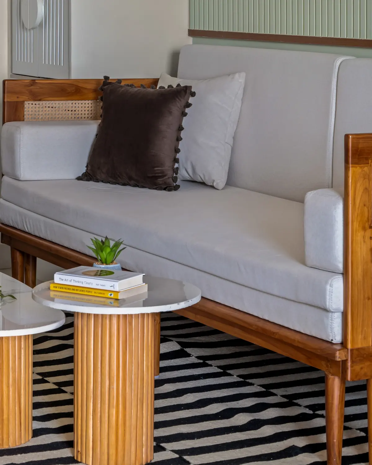 A teak sofa with woven cane sides and white cotton cushions, marble-topped tables in front.