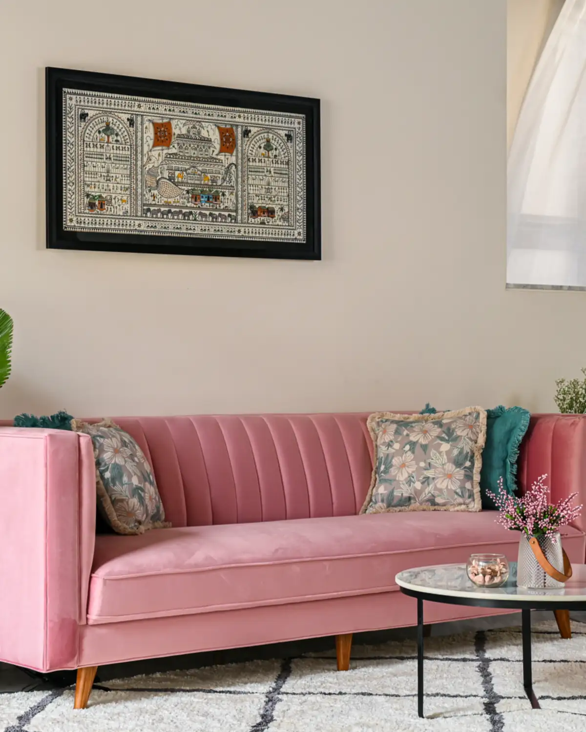A pink velvet sofa with a channel-stitched back on tapered teak legs, a folk painting above it.