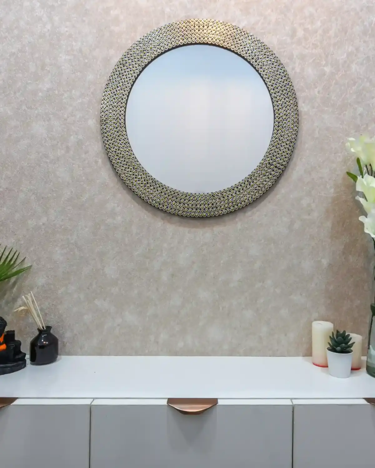 A round mirror in a wide hand-beaten metal frame above a white console.