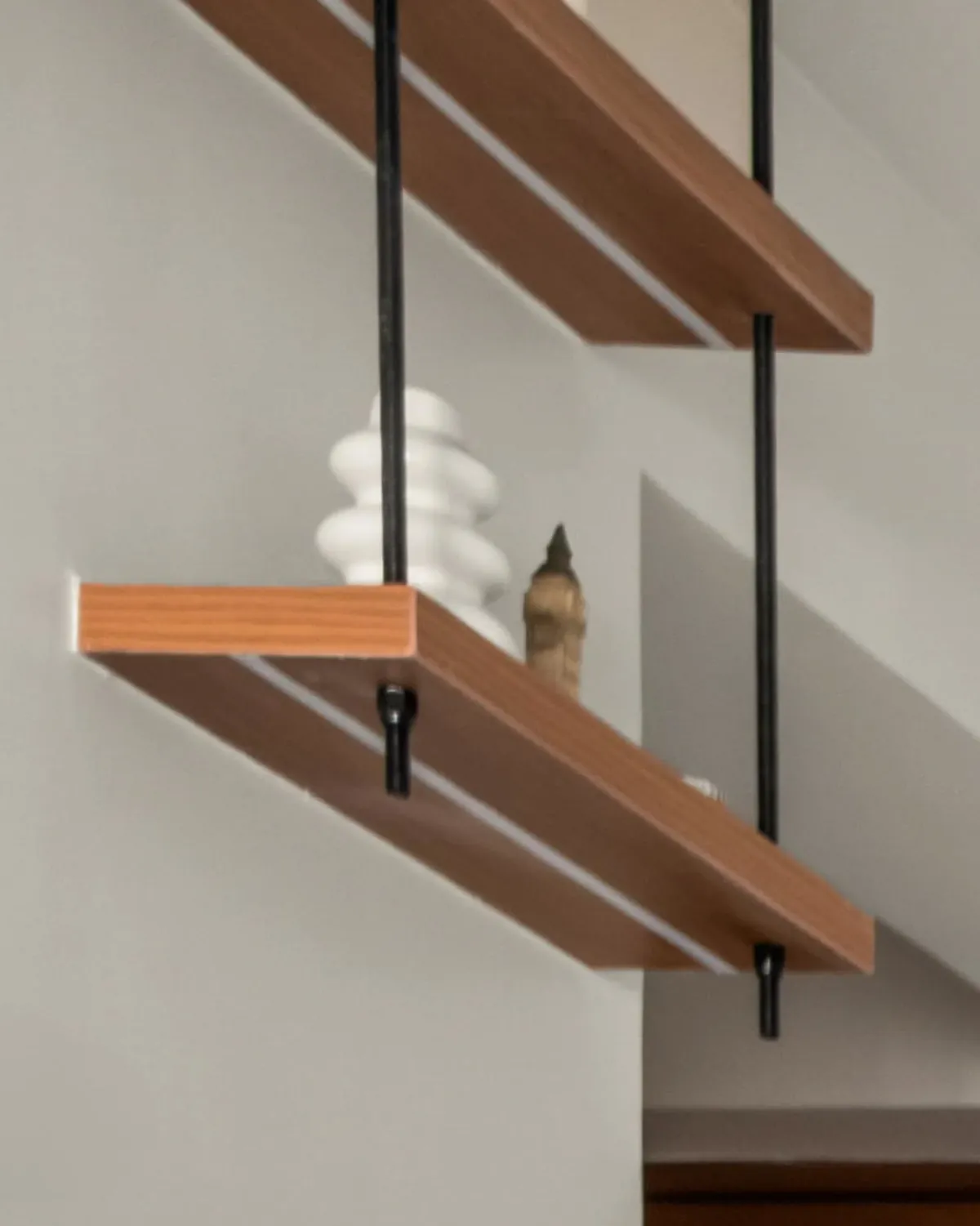 Two teak shelves hung from the ceiling on black steel rods, a white vase on the lower one.