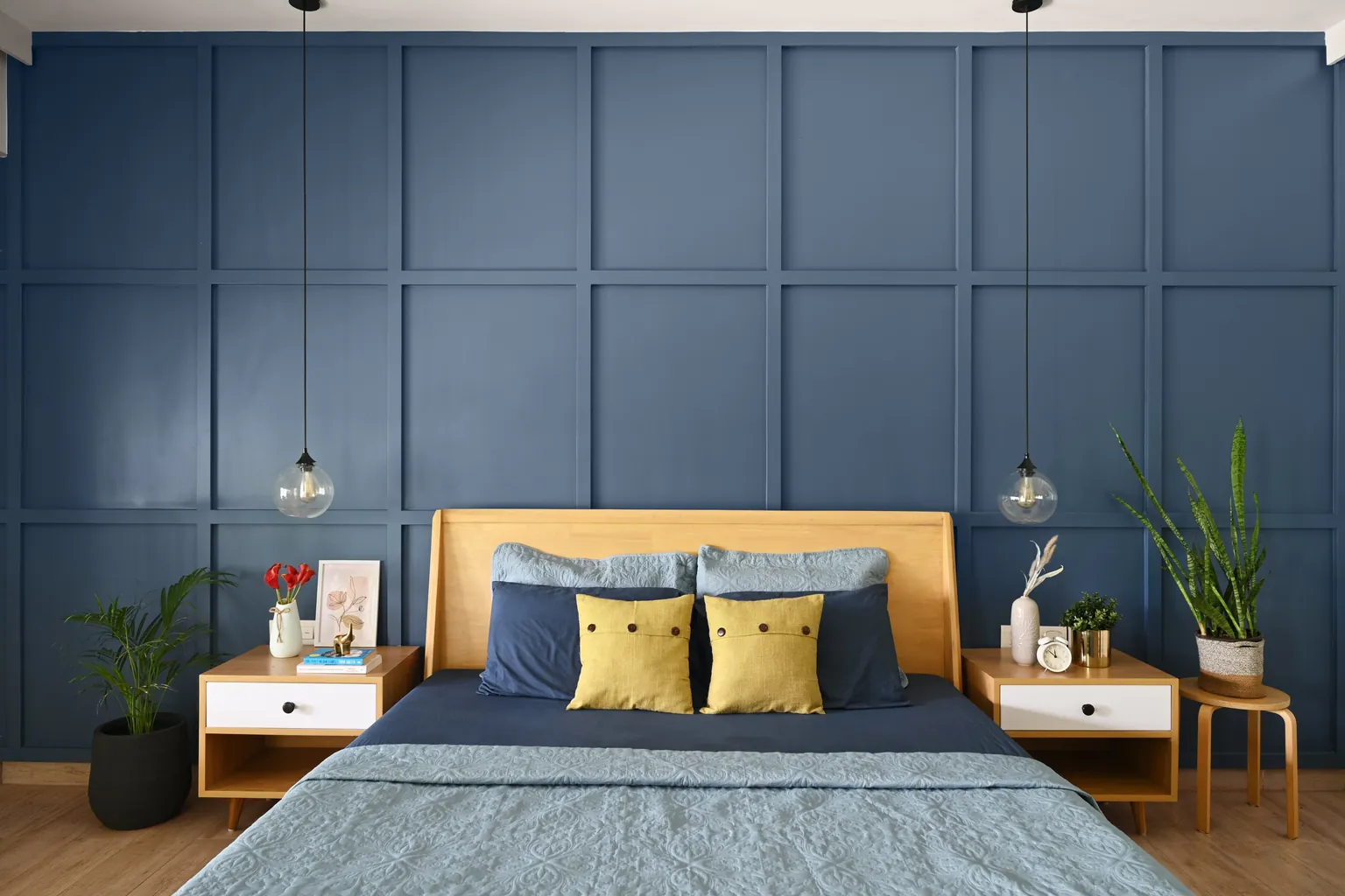 A bedroom with a teak bed against a blue panelled wall, a bedside table on each side and a glass pendant above each.