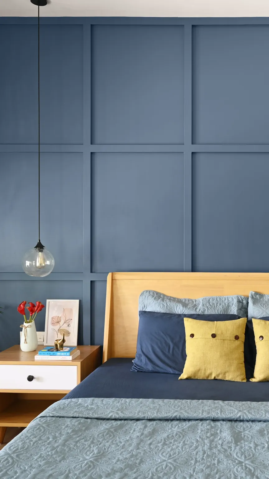 A bedroom with a teak bed against a blue panelled wall, a bedside table on each side and a glass pendant above each.
