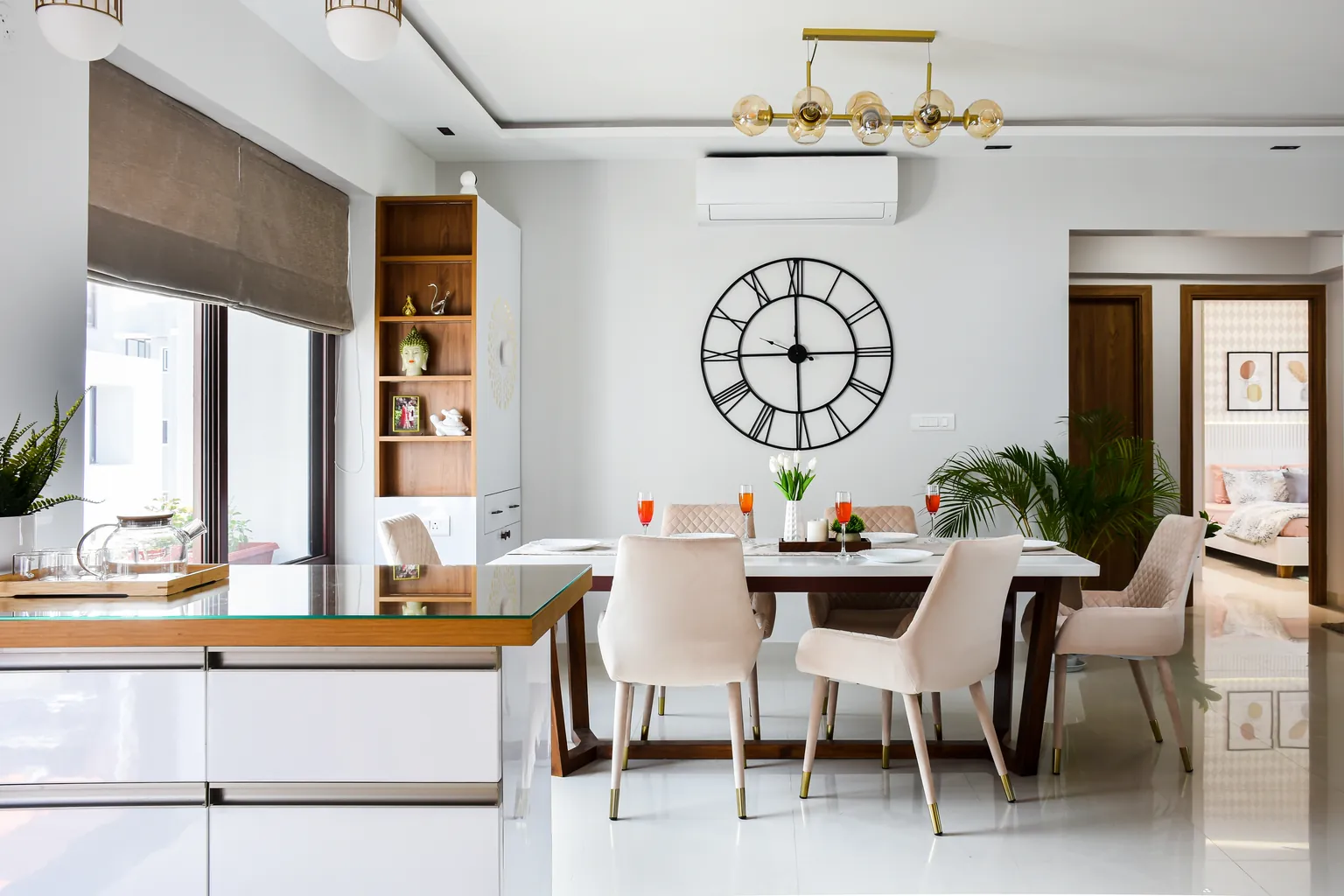 A dining room with a six-seater table, white marble on a sheesham trestle, cream velvet chairs and a brass pendant above.