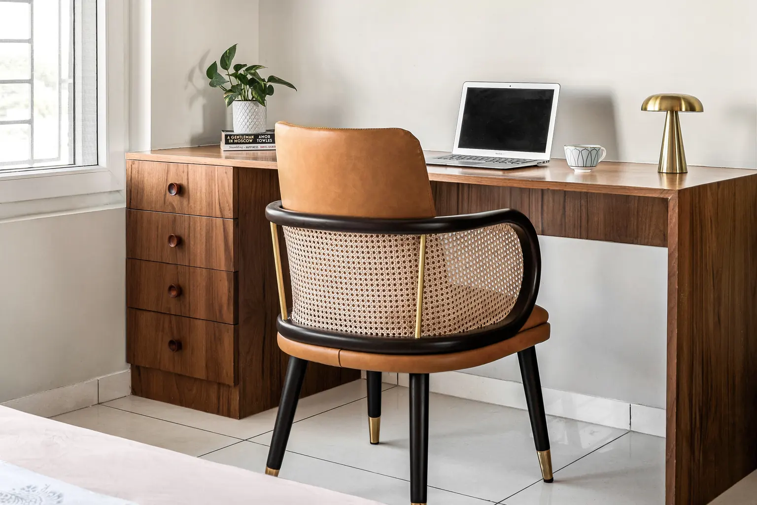 A study corner with a teak desk on a four-drawer pedestal and a cane-backed chair in a black frame.