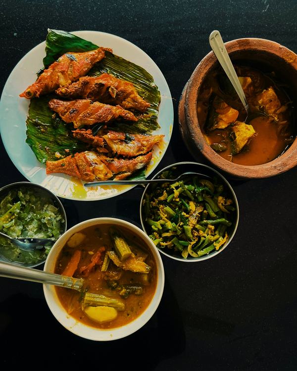 Chepala pulusu in a clay pot beside fried fish on a leaf and small bowls of curry.