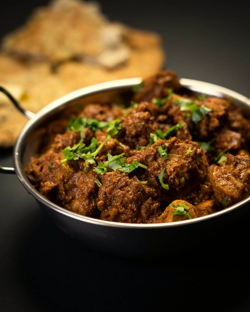 Gongura mamsam in a steel kadai, the mutton dark with gongura.