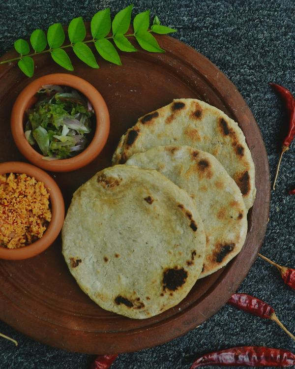 Jowar rotte on a wooden plate with podi and onion, dry red chillies around it.