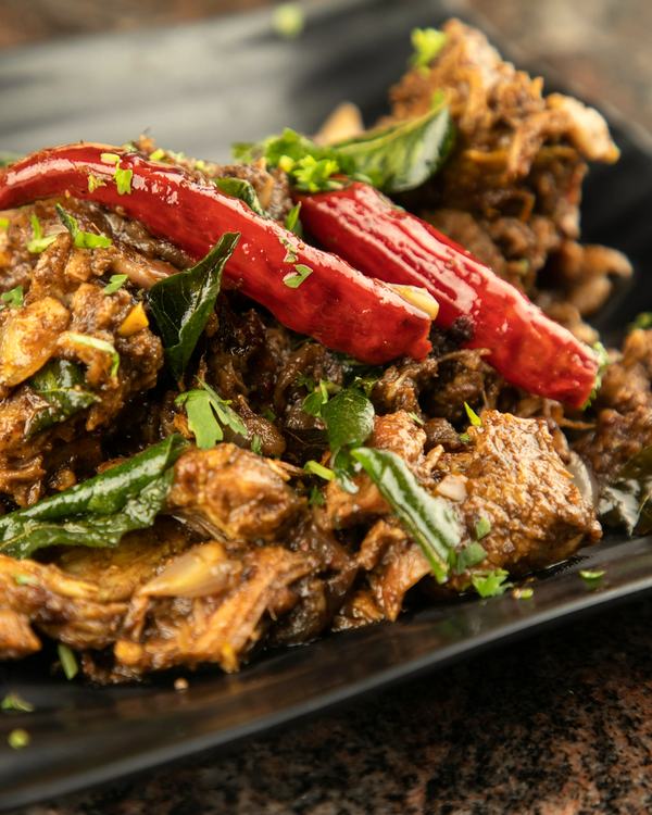 Kodi vepudu on a black plate, dry red chillies and curry leaves through it.