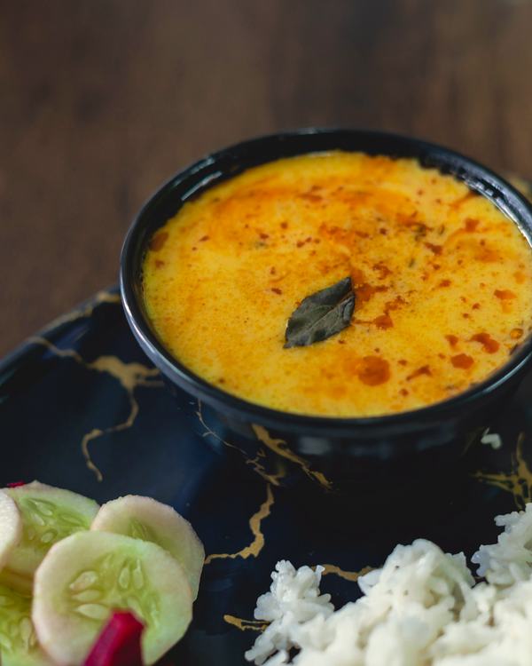 Majjiga pulusu in a black bowl, rice and cucumber beside it.