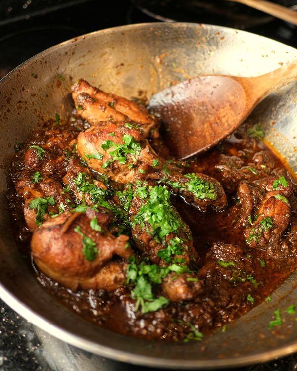 Natu kodi pulusu in a steel kadai, a wooden spoon in the gravy.