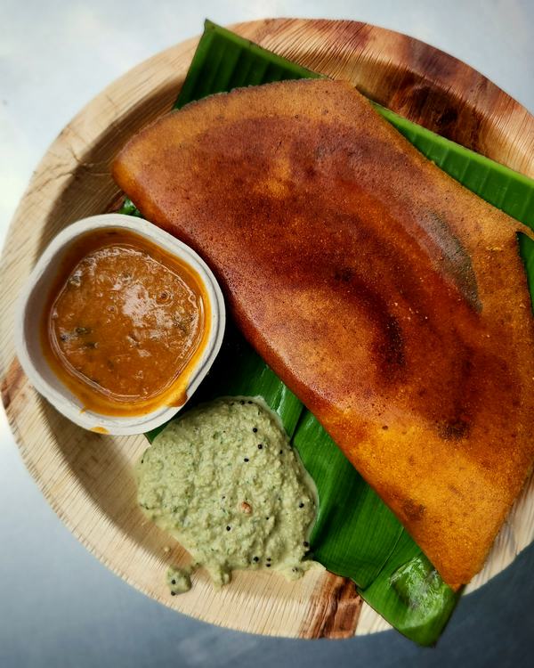 A neyyi dosa folded on a banana leaf, sambar and coconut chutney beside it.