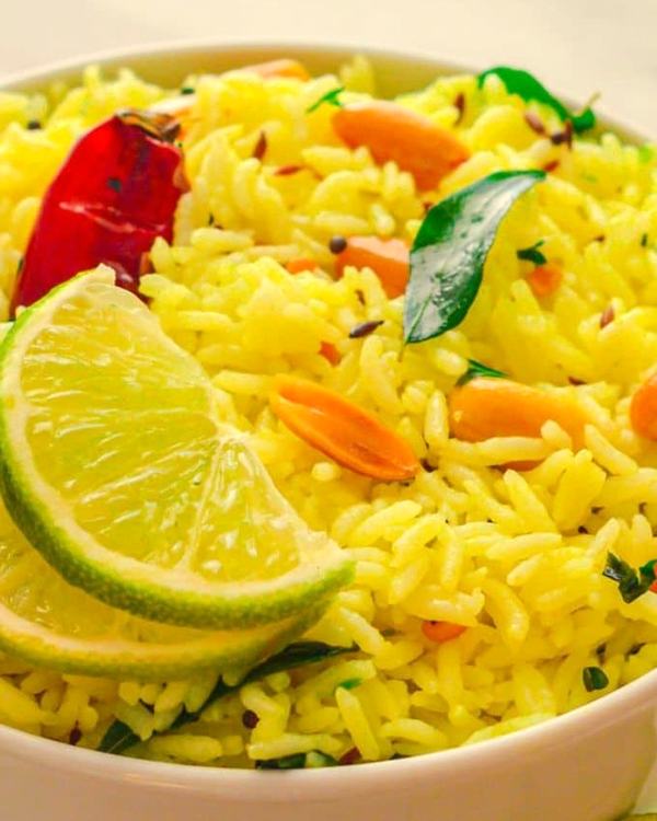 Nimmakaya pulihora in a bowl, a wedge of lime and cashews through the yellow rice.