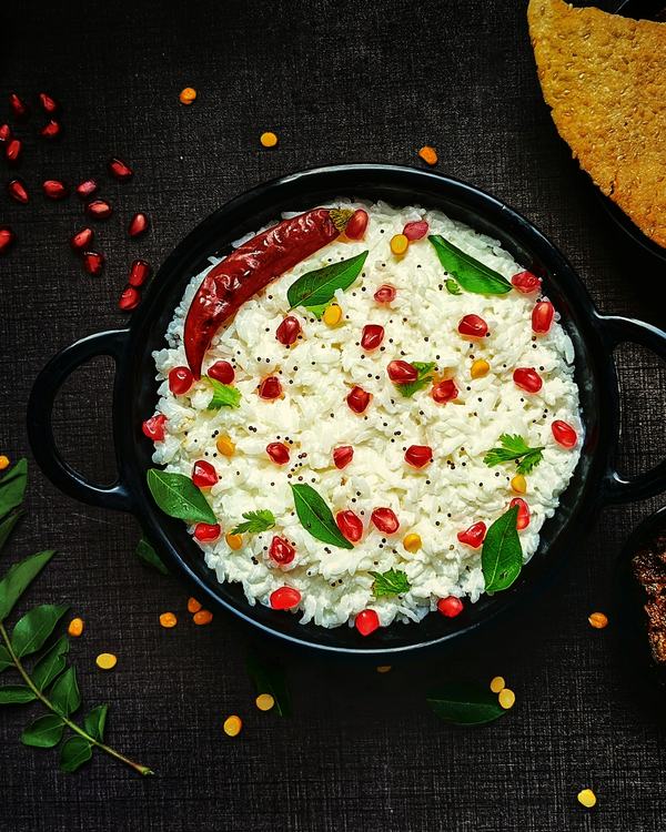 Perugu annam in a black pot, pomegranate and curry leaves over the curd rice.