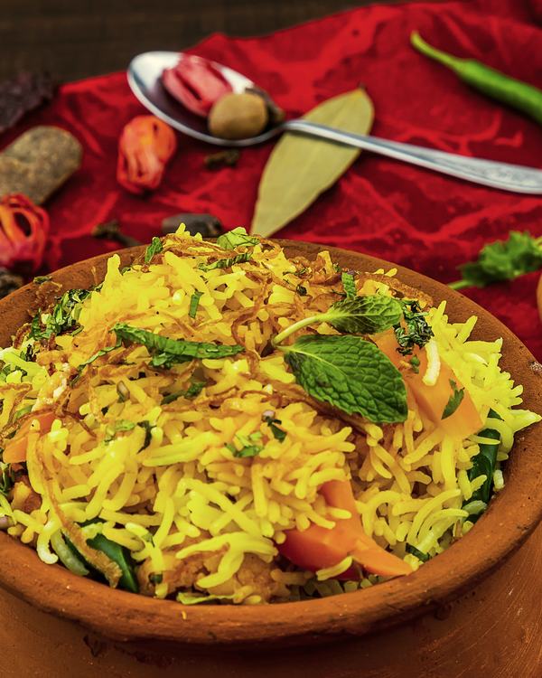 Veg biryani in a clay pot, a bowl of raita beside it.