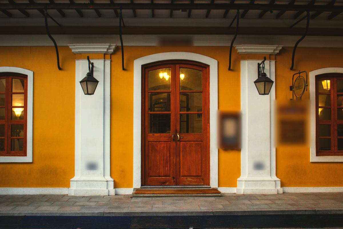 A wooden double door in a yellow wall, a lamp on either side.