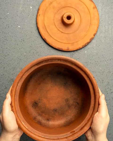 Two hands holding an empty clay pot, its clay lid above it.