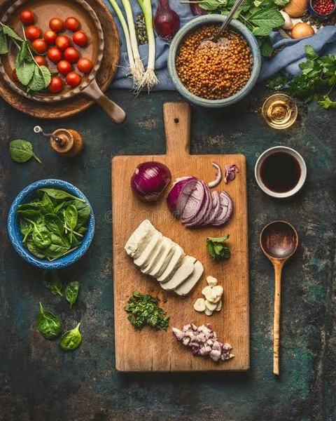Tomatoes, greens, onions, lentils and sliced paneer laid out around a chopping board.