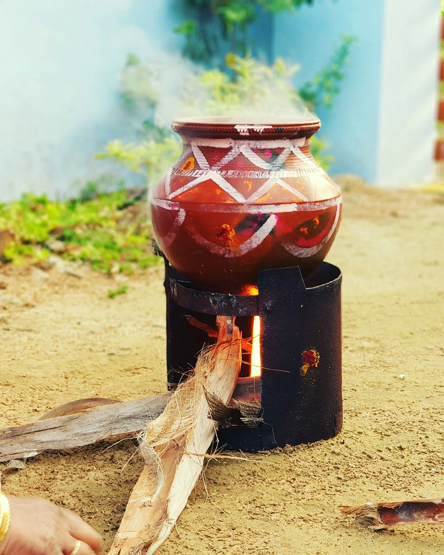 A painted clay pot on a small wood stove, steam at its mouth.