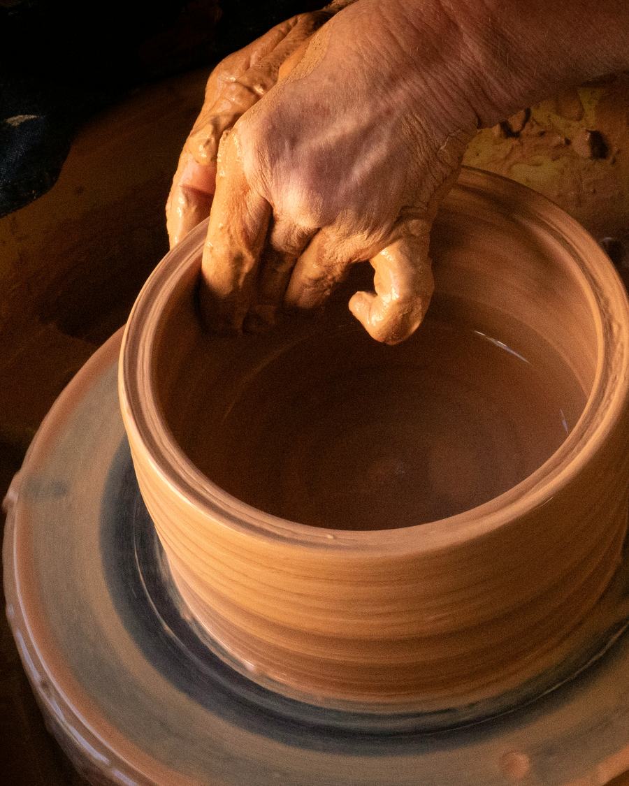 A potter's hands shaping a clay pot on the wheel.
