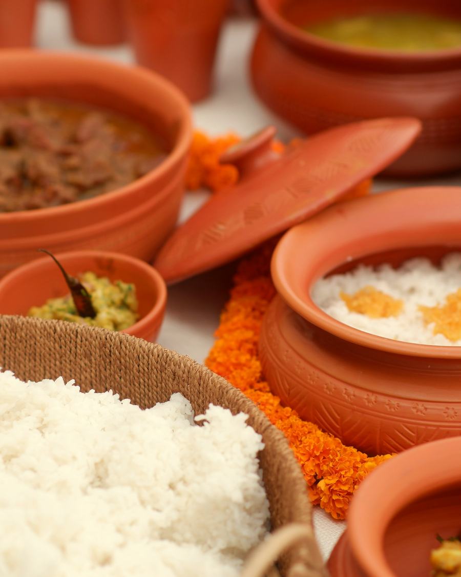 Curries, rice and curd served in clay pots on the table.