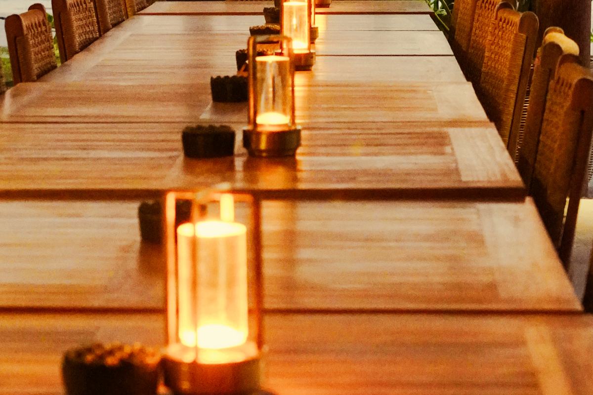 A long table at dusk, candles lit along it, cane chairs either side.
