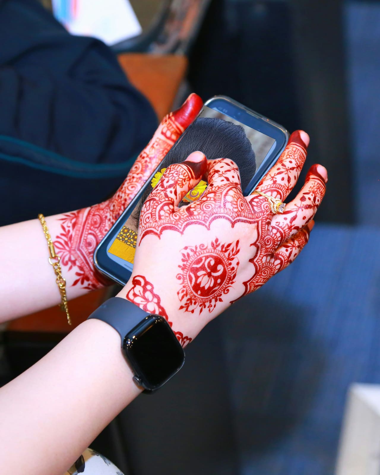Hands in red mehndi holding a phone, on its screen a photo of a bun pinned with marigolds.