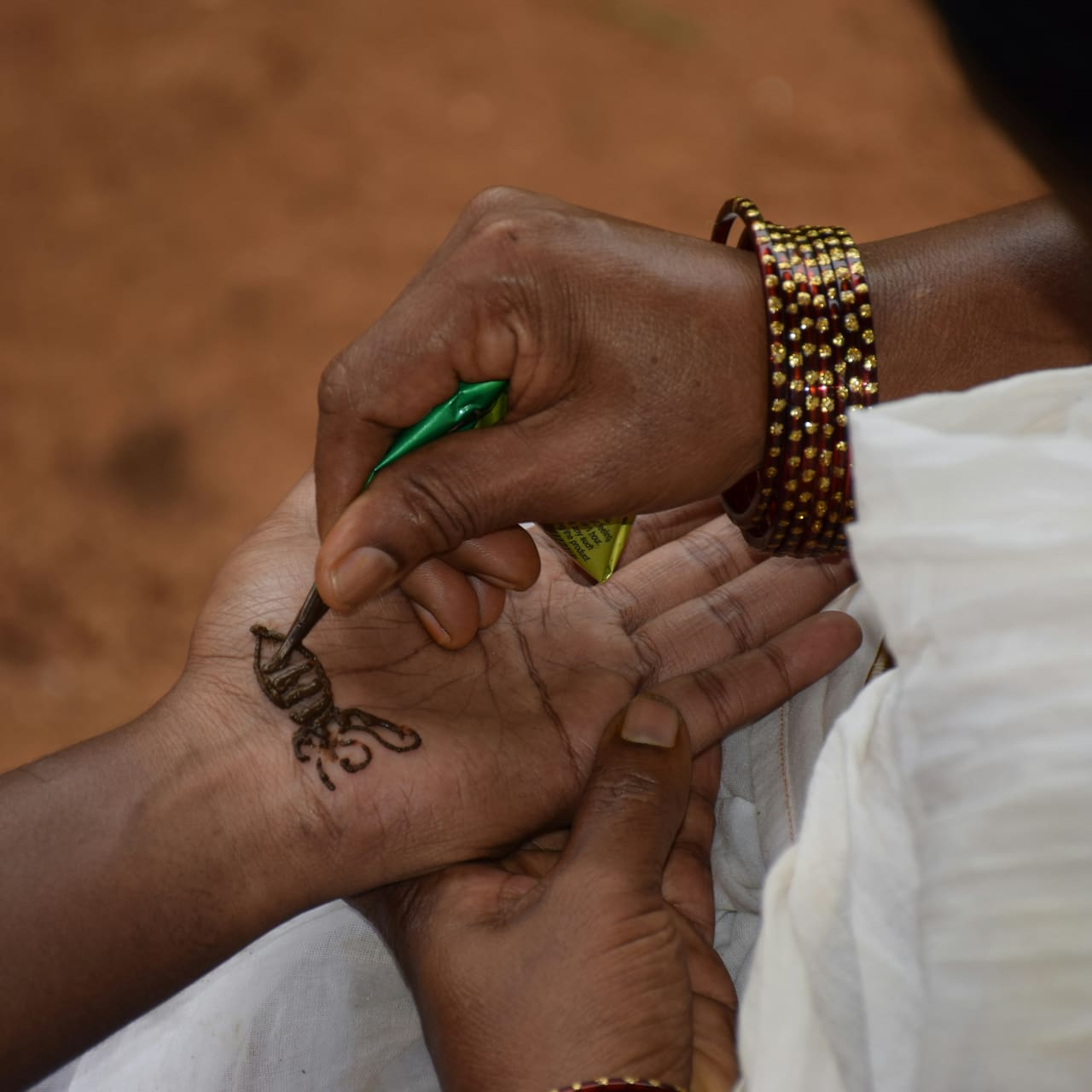 A mehndi cone drawing a pattern on a palm, the design half done.