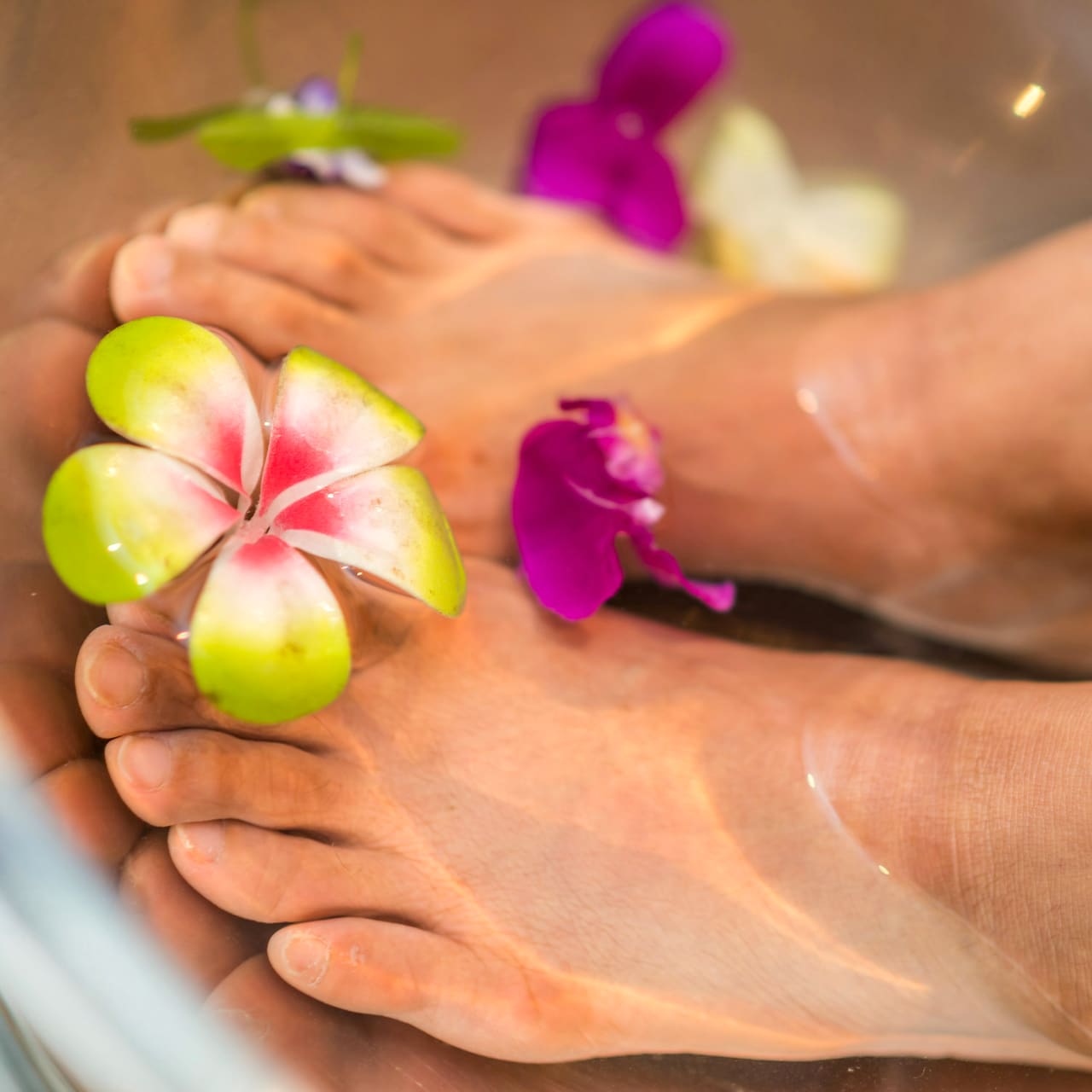 Feet in a pedicure basin, flowers floating in the water.